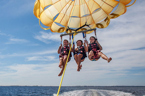 Three women enjoying a thrilling parasailing excursion with Gilligan's Watersports in Destin, Florida, which is available for free at Xplorie participating properties.