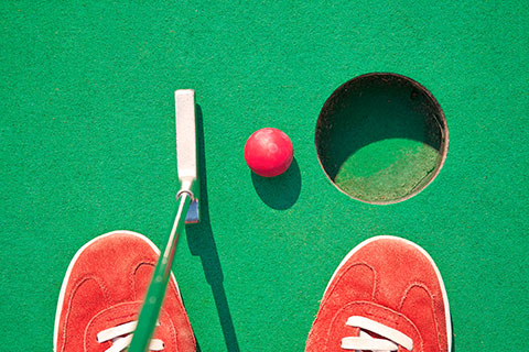 A person in red shoes about to putt a red ball into the hole at the mini golf course at Alpine Mini Golf in Helen, Georgia. Guests staying at Xplorie participating properties can enjoy a free round of mini golf.