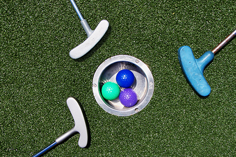Three putting golf clubs lay around a golf hole with colorful golf balls inside at Cape Escape Adventure Golf in Orleans, Massachusetts, where guests staying at Xplorie participating properties can enjoy a complimentary round of mini golf.