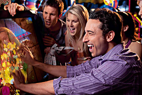 Group of friends playing an arcade game at Dave and Buster's in Panama City Beach, Florida, where guests staying at Xplorie participating properties can receive a free Twenty Dollar Power Card.