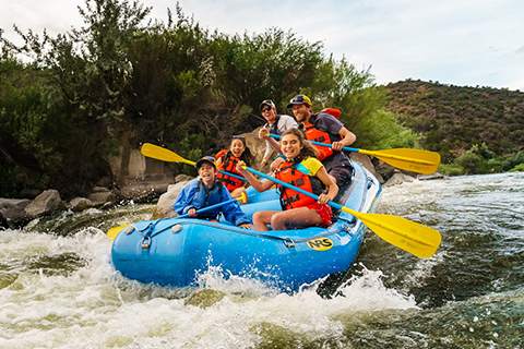 A family smiles as they enjoy a thrilling whitewater rafting adventure from Far Flung Adventures in Embudo, New Mexico, which guests staying at Xplorie participating properties can enjoy for free.