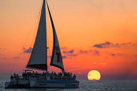 Group of people viewing a beautiful fiery sunset on the Island Time Sunset & Dolphin Watch Sailing Cruise in Panama City Beach, Florida, which is available free to guests staying at Xplorie participating properties.