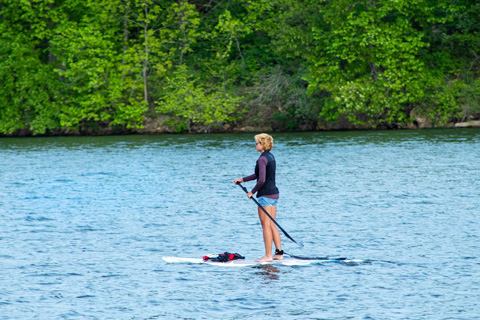 A woman enjoying a SUP on a lake with a rental from Jordanelle Rentals and Marina in Heber City, Utah, which is available for free to guests staying at Xplorie participating properties.