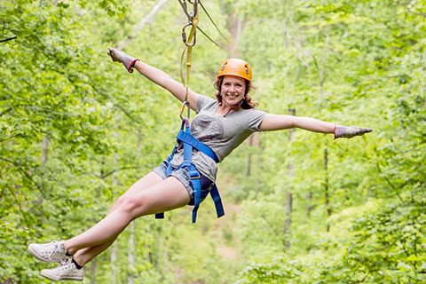 A woman holds her arms out and grins while ziplining with Legacy Mountain Zip Lines in Sevierville, Tennessee, which is available for free to guests staying at Xplorie participating properties.