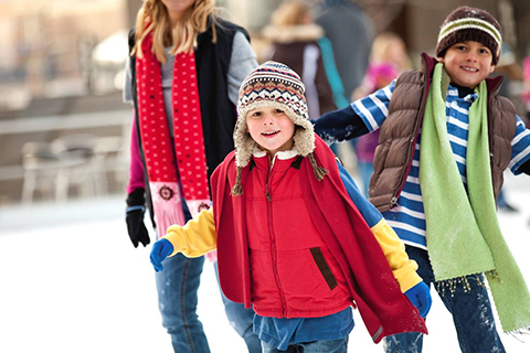 A family enjoys ice skating at the Resort Center Ice Skating Rink in Park City, Utah, where guests staying at Xplorie participating properties can enjoy a free general admission to ice skating with rental skates included.