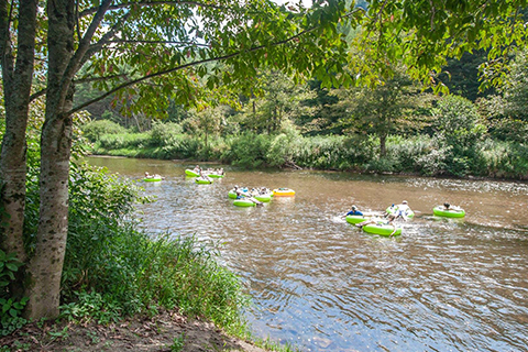 A group of people enjoy a leisurely tubing float down the river with a tubing excursion from River & Earth Adventures in Todd, North Carolina, where guests staying at Xplorie participating properties can enjoy for free.