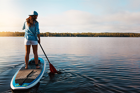 A woman paddles along still waters at sunrise with a paddleboard rental from Sunriver ToyHouse Toys in Sunriver, Oregon, which guests can enjoy for free when staying at an Xplorie participating property.